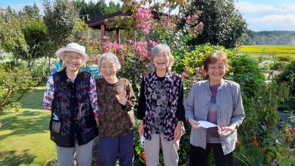 庭園で4人の入居者が花を背景に笑顔で記念撮影している様子
